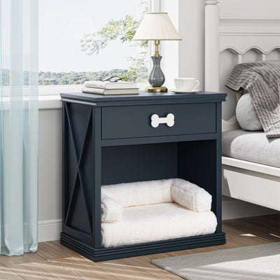 Navy blue pet bed with white cushion next to a nightstand with a lamp and books in a bedroom.