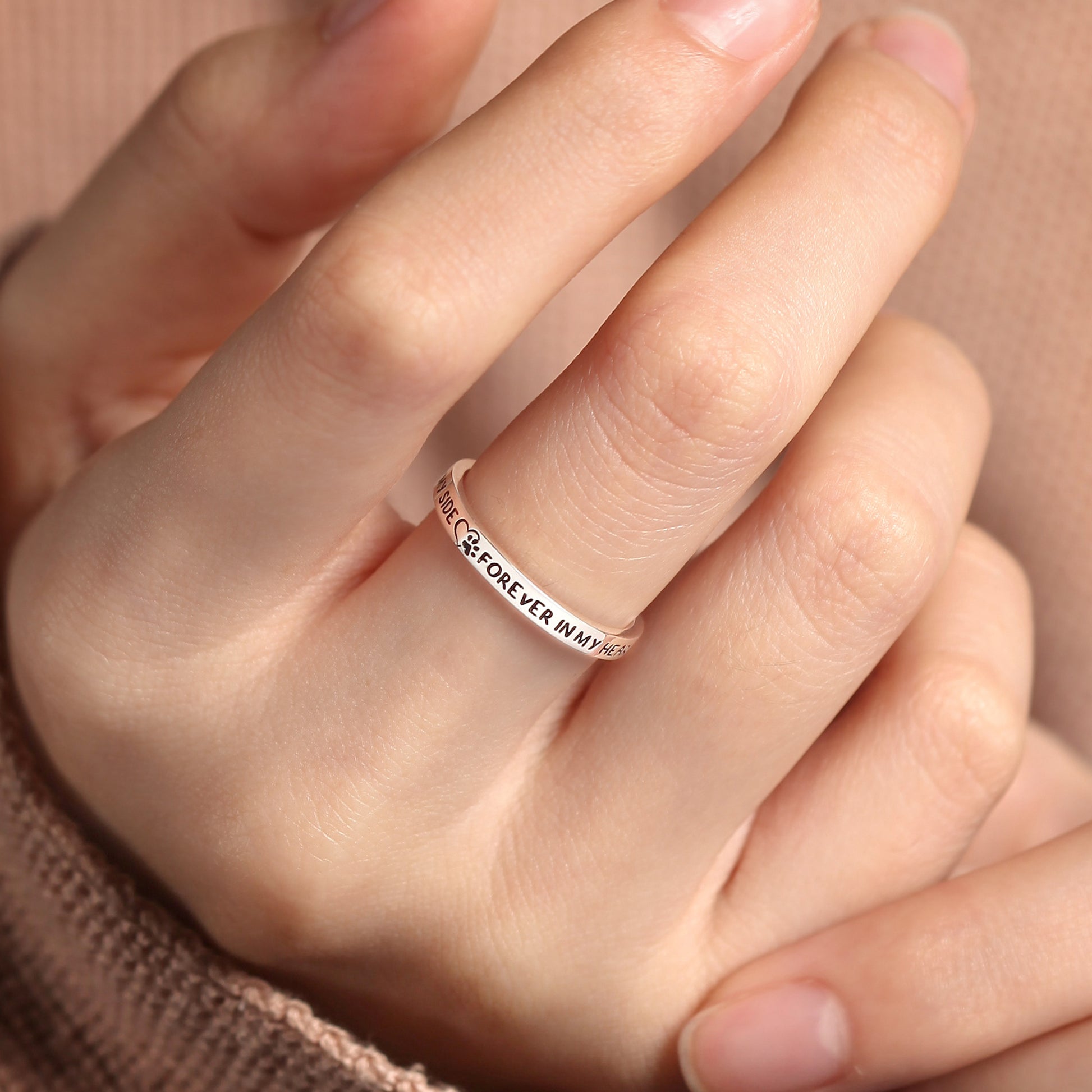Silver ring with engraved text on a person's finger against a neutral background