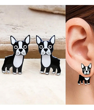 Black and white dog-shaped earrings on a wooden surface and worn on an ear.